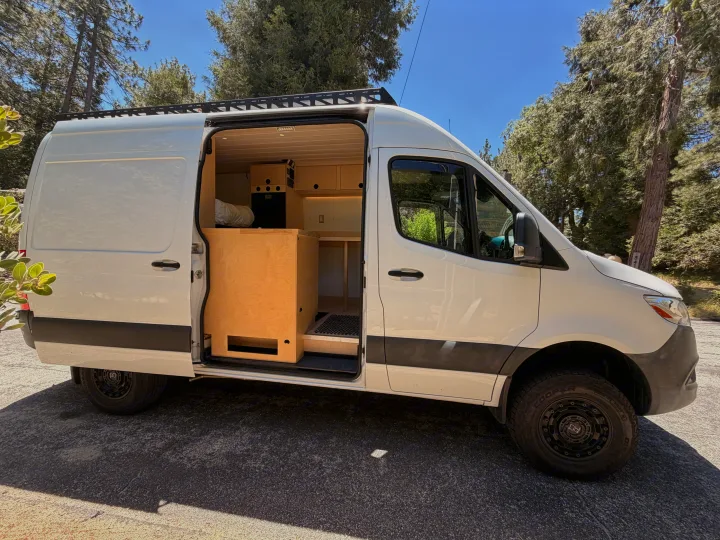 White custom camper van with open side door showcasing its wood interior. Ideal for your next RV rental adventure.. Mercedes-Benz Sprinter 2019