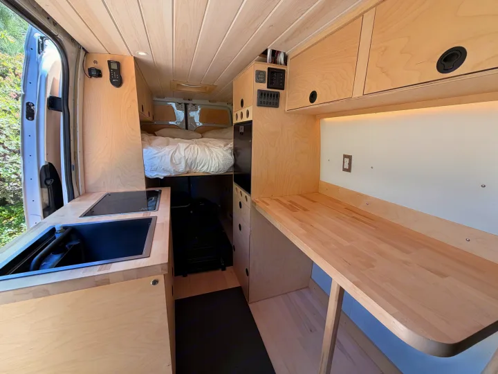 Spacious rv rental interior featuring a wood-paneled van conversion with a kitchenette, bed, and work counter for comfortable travel.. Mercedes-Benz Sprinter 2019