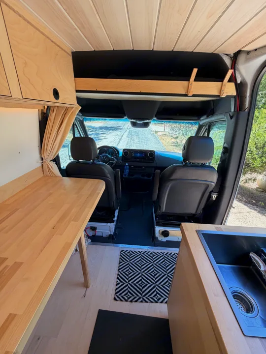 RV rental: View inside a custom camper van showing a wood kitchen, dining table, and front driver's cabin.. Mercedes-Benz Sprinter 2019