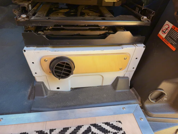 RV rental camper van interior featuring a passenger swivel seat base over a functional heater vent with wooden trim, enhancing comfort.. Mercedes-Benz Sprinter 2019