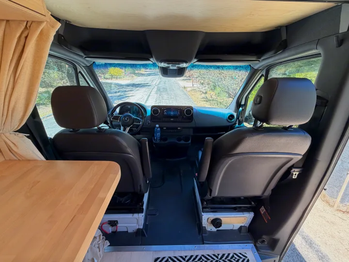 RV rental camper van interior. View from living area to front cockpit with dashboard, steering wheel, seats & wooden ceiling.. Mercedes-Benz Sprinter 2019