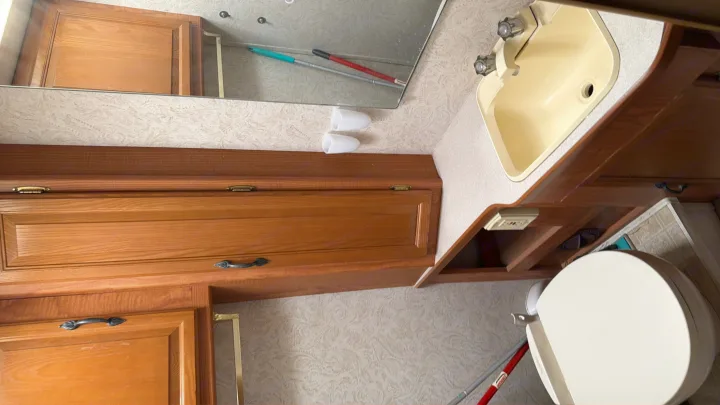 RV rental bathroom interior: Compact space with wood cabinets, a beige sink, mirror, and white toilet.. Coachmen Leprechaun 2003