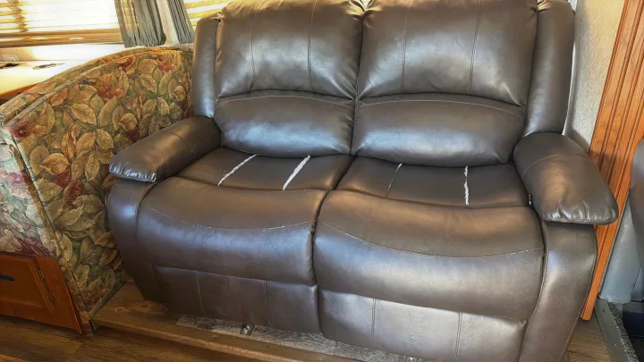 Brown two-seat recliner sofa with peeling faux leather cushions, next to a floral patterned bench, inside an RV rental.. Coachmen Leprechaun 2003