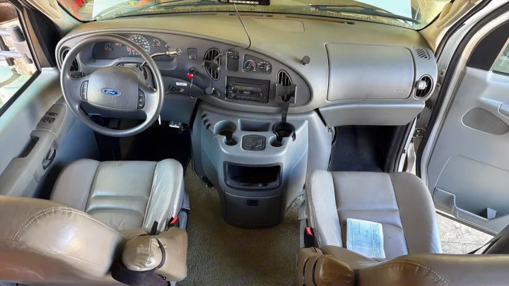 RV rental van's interior: a wide view of the gray dashboard, Ford steering wheel, console with cup holders, and front seats.. Coachmen Leprechaun 2003