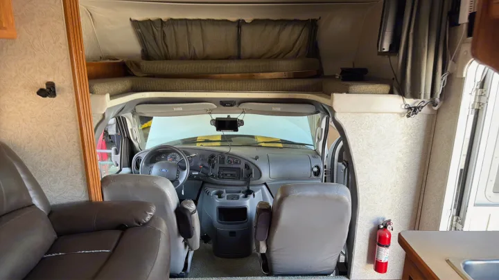 RV rental interior featuring the cockpit, overhead bed, front seating, and a mounted fire extinguisher for safety.. Coachmen Leprechaun 2003
