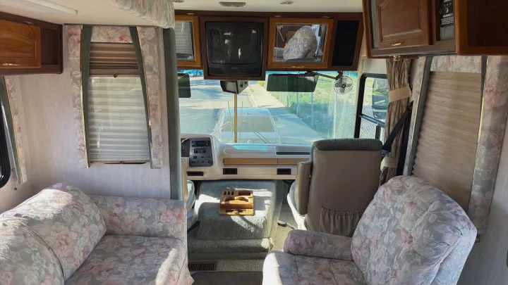 Get a glimpse inside this charming rv rental. Featuring floral-patterned seating, a dashboard view, and a classic TV setup.. Intermountain Rv TROPICAL 1997