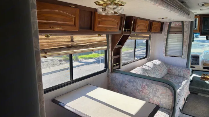 Step into this cozy rv rental: A vintage RV interior with wooden cabinets, a floral sofa, dinette, and bright windows.. Intermountain Rv TROPICAL 1997