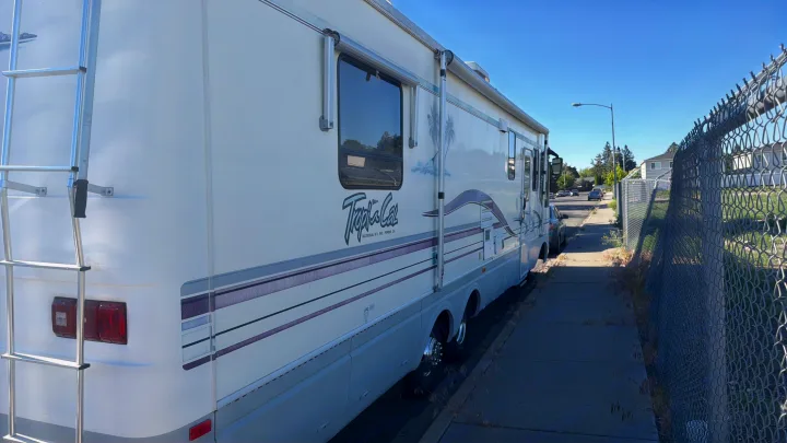 White Tropical RV rental motorhome parked curbside on a sunny day, visible past a chain-link fence.. Intermountain Rv TROPICAL 1997