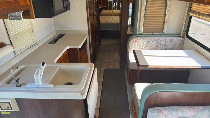 View of an rv rental interior showing kitchen, floral dinette seating, and hallway leading to the bed.. Intermountain Rv TROPICAL 1997