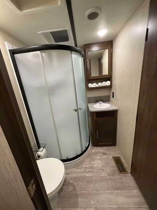 RV rental bathroom: compact design with a curved shower stall, toilet, sink vanity with mirror, and towel storage.. Crossroads RV Volante 2020