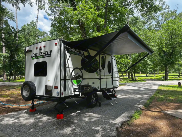 This rv rental, a white Remote Coachmen travel trailer, is parked and set up at a shaded campsite, ready for adventure.. Coachmen RMT18R 2024