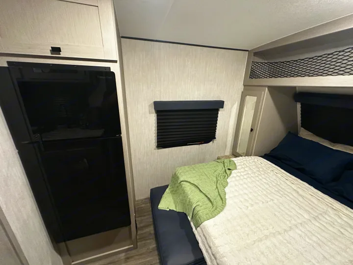 RV rental bedroom: a cozy interior featuring a bed, refrigerator, mirrored wardrobe, and practical overhead storage.. Coachmen RMT18R 2024