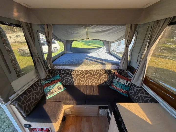 Cozy pop-up rv rental interior, with a comfy bed, lounge seating, and bright window views for camping trips.. Outback Eagle Off-Road 2015