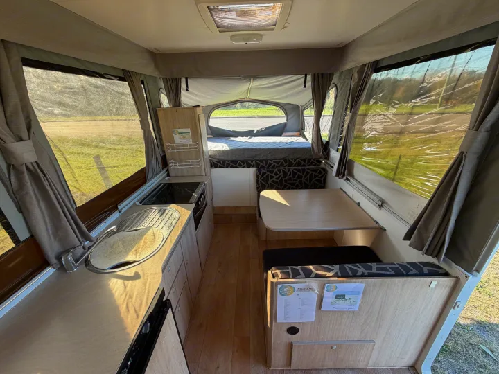 Bright pop-up camper **rv rental** interior, showcasing a compact kitchen, dining area, and cozy bed with scenic views.. Outback Eagle Off-Road 2015