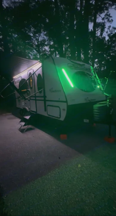This Coachmen RV rental, illuminated by green and white LED lights at a campsite, offers a unique night camping experience.. Coachmen RMT18R 2024