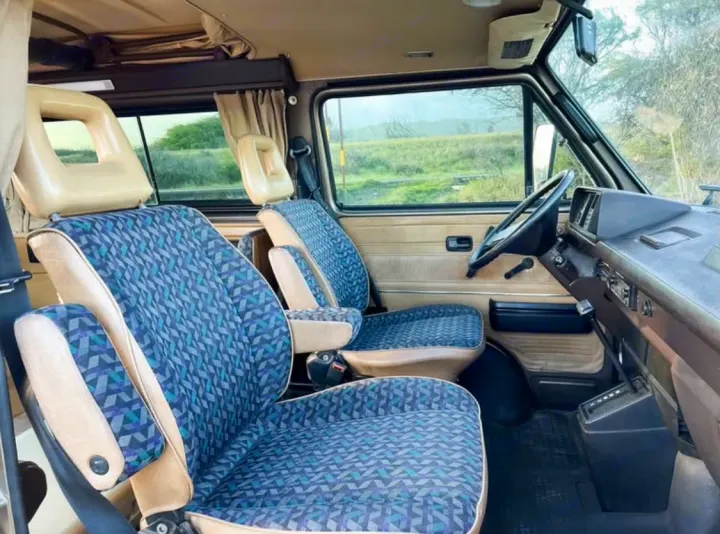 Inside a charming rv rental campervan, featuring unique patterned seats, dashboard, and a view of nature.. Volkswagen Westfalia 1985