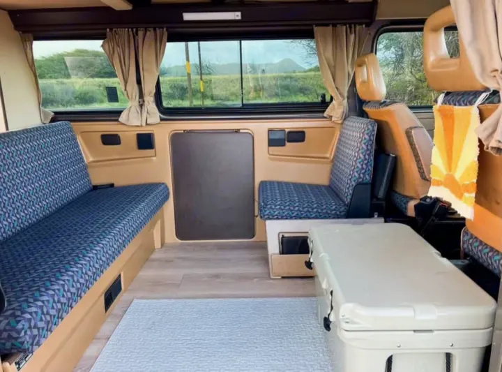 Inside an RV rental: patterned bench seating, fold-down table, and cooler, with a view of mountains from the windows.. Volkswagen Westfalia 1985