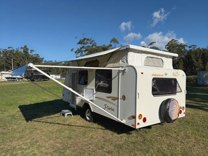 White Jayco pop-top caravan (rv rental) with awning extended, parked on grass under a blue sky. Ready for adventure!. Jayco J Series 2008