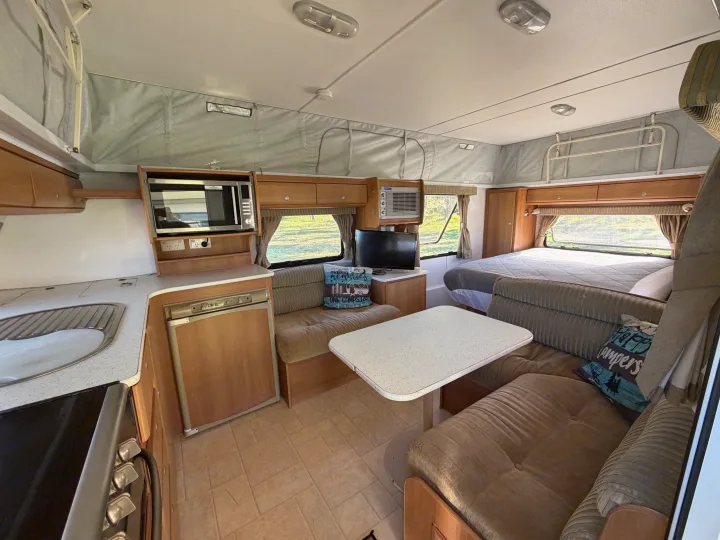 Inside a pop-top rv rental, showing a kitchen, dining booth, and bed. A well-equipped, cozy space for road trips.. Jayco J Series 2008