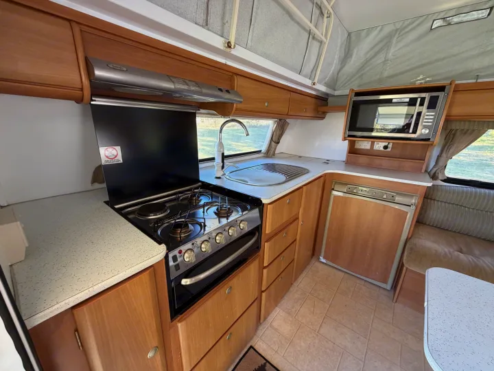 This RV rental shows a compact kitchen with a stove, oven, sink, microwave, fridge, and wooden cabinets in a pop-top camper.. Jayco J Series 2008