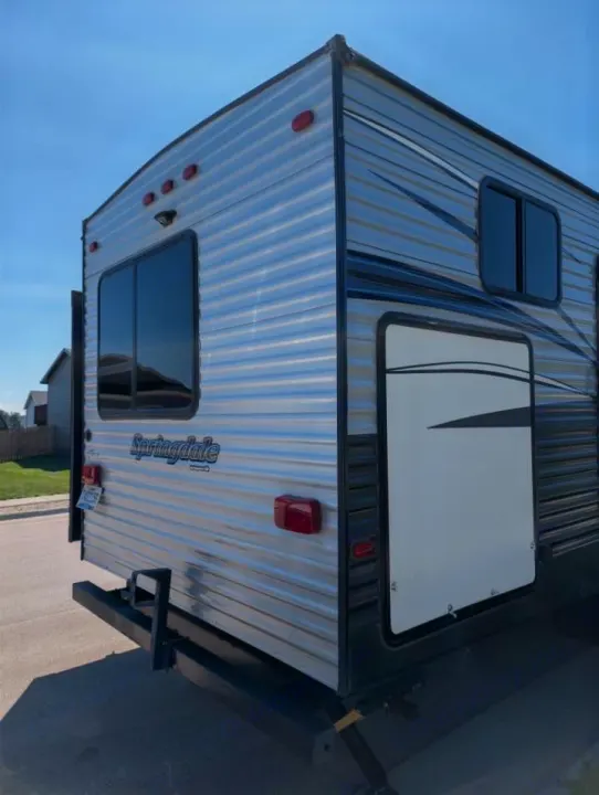 Rear and side view of a Springdale RV rental, silver with black trim, featuring windows and tail lights under a blue sky.. Keystone RV Springdale 2019