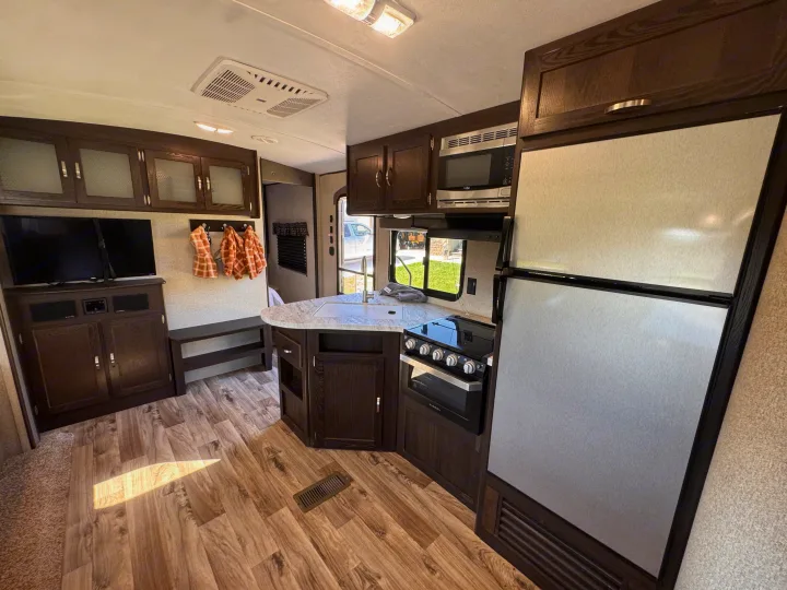 Modern rv rental interior: dark wood cabinetry, kitchen with sink, stove, microwave, fridge, plus TV area & wood-look floor.. Keystone RV Springdale 2019