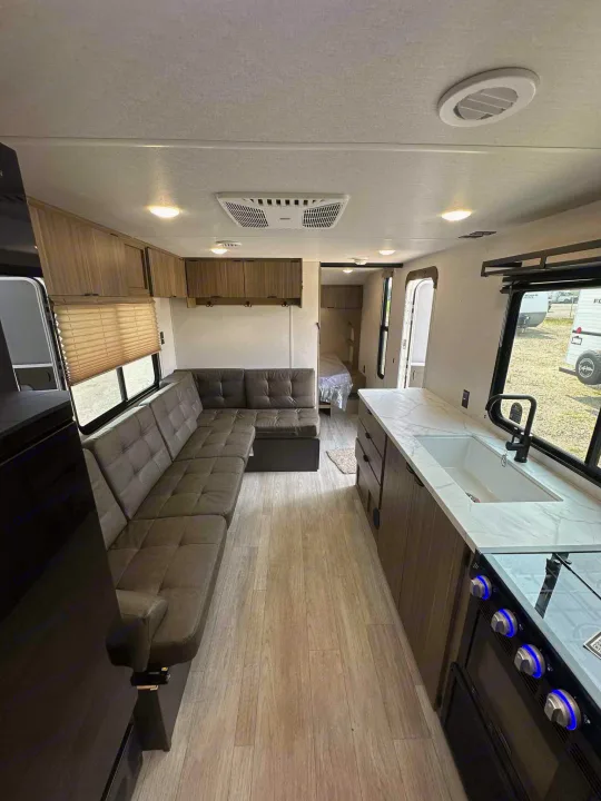 Modern rv rental interior: L-shaped sofa, full kitchen with stove/sink, and back bedroom. Bright, wood-look flooring.. Forest River Salem FSX 266BHLE 2026