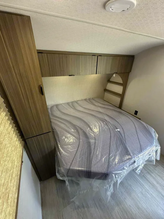 Modern RV rental bedroom featuring a protected mattress, ample wood-finish cabinetry, and a clean interior. Ideal for your travels.. Forest River Salem FSX 266BHLE 2026