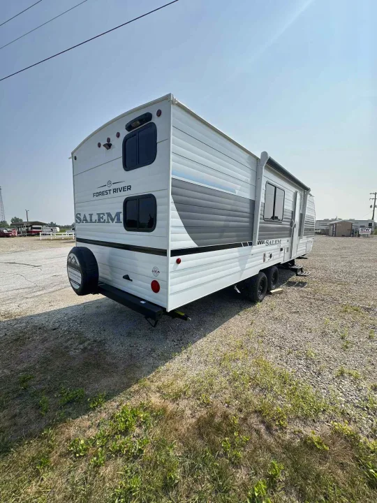 A white Forest River Salem travel trailer, perfect for rv rental, with gray accents and a spare tire, parked on a sunny gravel lot.. Forest River Salem FSX 266BHLE 2026