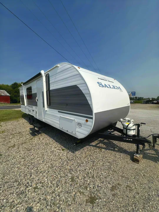 This white and gray travel trailer is ready for your next RV rental adventure, parked on gravel under a clear sky.. Forest River Salem FSX 266BHLE 2026