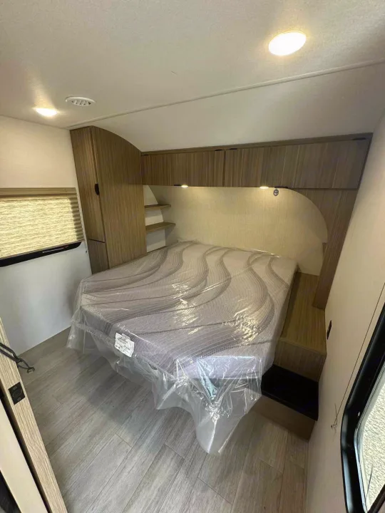 Bright RV rental bedroom: cozy bed with plastic cover, modern cabinetry, shelving, and window with blinds.. Forest River Salem FSX 266BHLE 2026