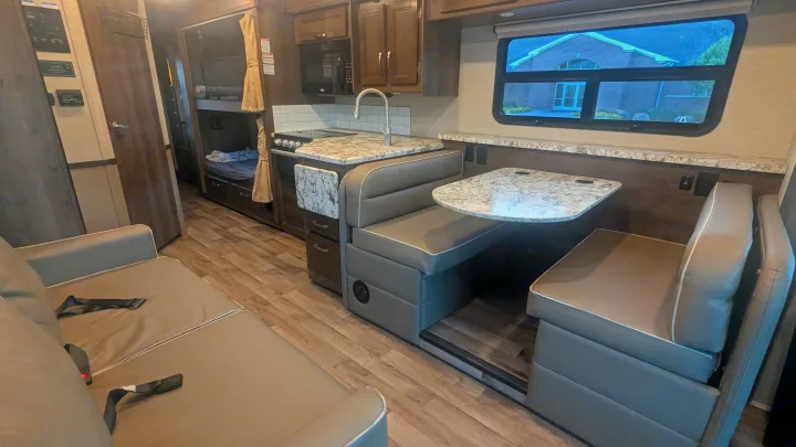 This RV rental interior features a kitchen, dinette, sofa with seatbelts, and bunk beds, offering a comfortable travel space.. Jayco Alante 2020