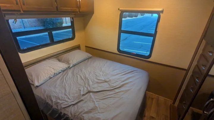 Experience comfort in this RV rental bedroom: grey bed, two windows, overhead storage, and wood floor.. Jayco Alante 2020