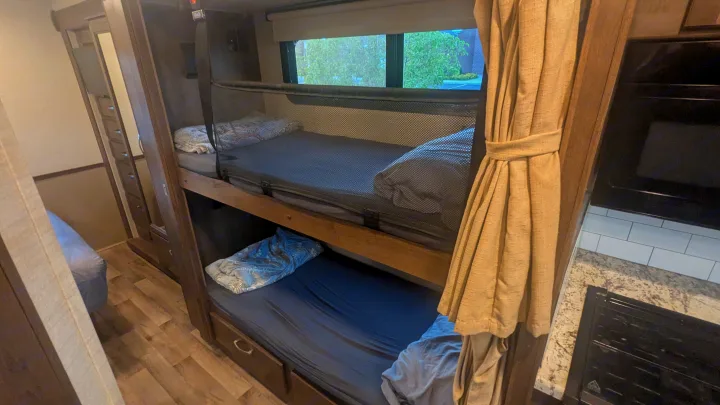 This RV rental offers practical bunk beds with safety nets, a mirrored wardrobe, and a peek at the kitchen, perfect for travel.. Jayco Alante 2020