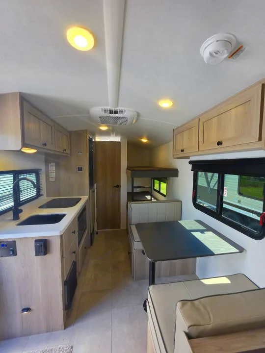 Modern rv rental interior: kitchen with sink, dinette, and bunk beds. Bright cabin with light wood cabinetry, ready for your adventure.. Forest River Rockwood Geo Pro 2026