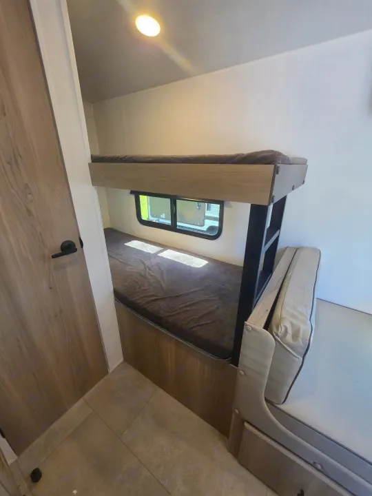 Inside an RV rental: view of light-wood bunk beds with dark gray bedding, a window, and a tan upholstered bench.. Forest River Rockwood Geo Pro 2026