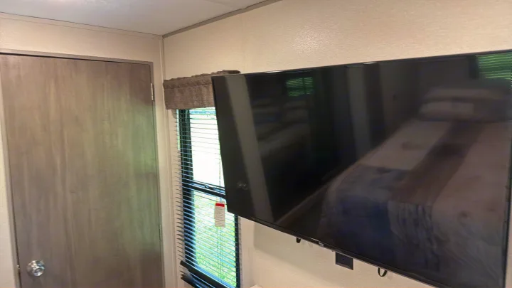 Modern RV rental interior: Mounted TV, door, and window with blinds. Bed reflection is visible on the screen.. Coachman Catalina, Legacy edition 343BHTS 2024