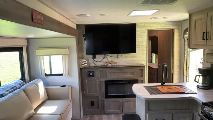 Modern rv rental interior: cozy living area with sofa, fully-equipped kitchen, TV, & fireplace for a comfortable camping trip.. Coachman Catalina, Legacy edition 343BHTS 2024