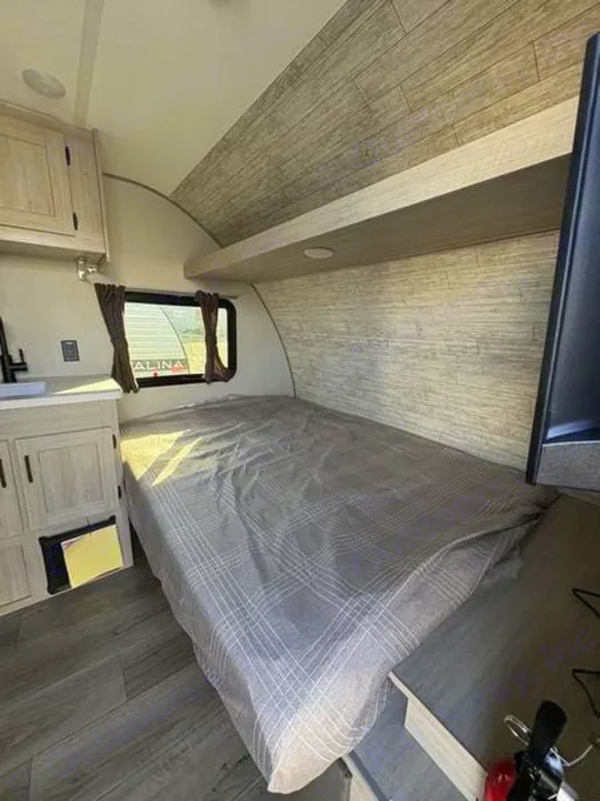 RV rental interior featuring a compact bedroom with a gray patterned bed, wood-look walls, cabinet storage, and a small window.. 5ZT2CABC9TK012992 Catalina 2026