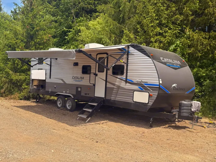 Experience nature with this Catalina Legacy Edition RV rental, parked on gravel with awning extended at a green campsite.. Coachmen Other 2021