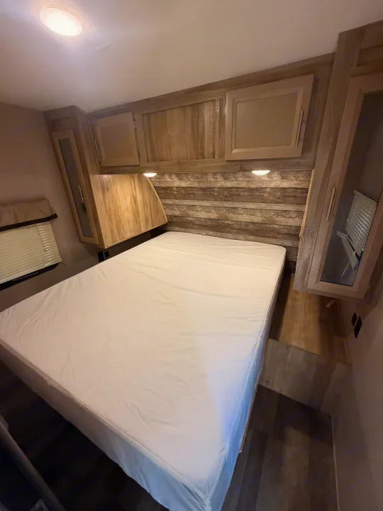 Cozy RV rental bedroom features a comfortable bed, wood paneling, overhead cabinets, and a window with blinds.. Coachmen Other 2021