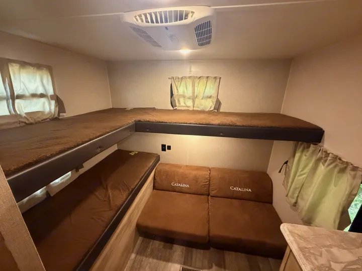 This rv rental offers cozy L-shaped bunk beds with brown cushions and a Catalina-branded seating area, perfect for family adventure.. Coachmen Other 2021