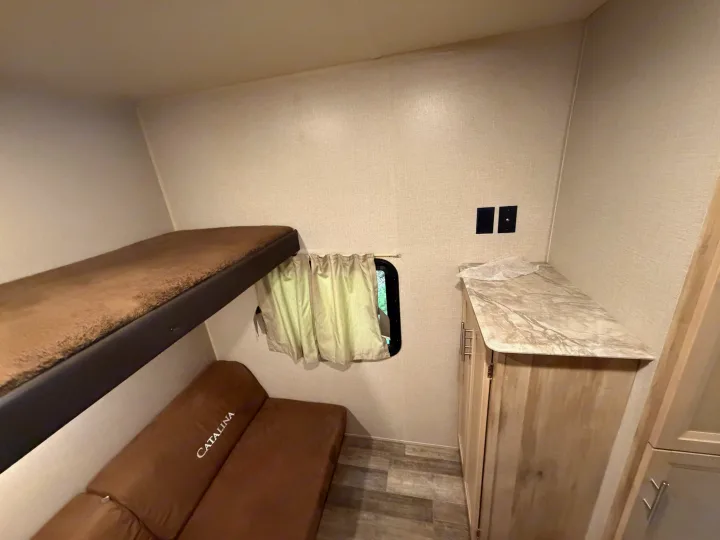 Cozy RV rental interior featuring a bunk bed, sofa, window with curtains, and storage cabinet. Ideal for compact living.. Coachmen Other 2021
