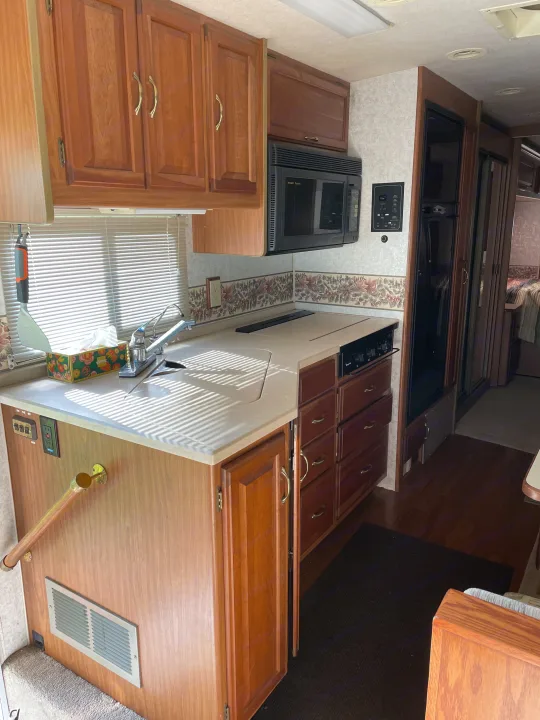 Interior of an RV rental kitchen showcasing wooden cabinetry, a light countertop with sink, built-in stove, microwave, and fridge.. Winnebago Chieftain 1999