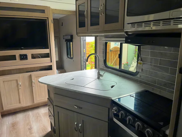 Spacious RV rental kitchen featuring a sink, stove, microwave, and entertainment center. Ready for your travels!. Coachmen freedom express 2021