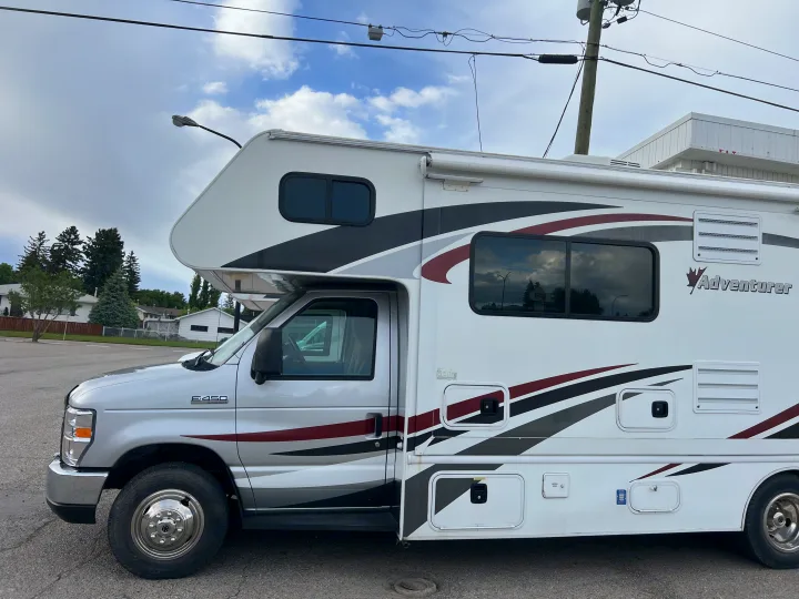 Side view of a white & silver Class C Adventurer E-450 rv rental with red and black graphics, parked outdoors.. Adventurer Adventurer Motorhome 2016