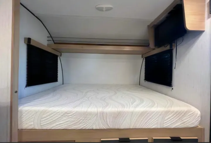 Clean RV rental bedroom featuring a comfy mattress, black window blinds, overhead shelf, and a wall-mounted TV.. Cruiser RV Hitch 2022