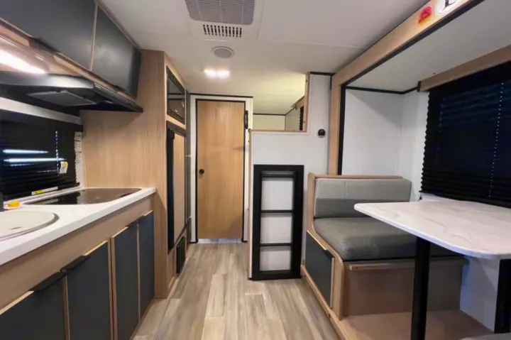 This modern RV rental interior features a kitchen with a stovetop, sink, microwave, and a cozy dinette with seating.. Cruiser RV Hitch 2022