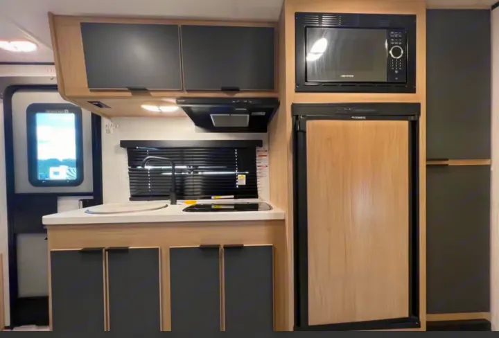 This RV rental kitchen features a microwave, Dometic fridge, sink, and cooktop, with modern dark and light wood cabinetry.. Cruiser RV Hitch 2022