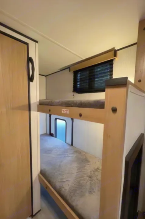 Inside an rv rental: sturdy bunk beds with grey mattresses, a top window, and a bright lower window for light.. Cruiser RV Hitch 2022